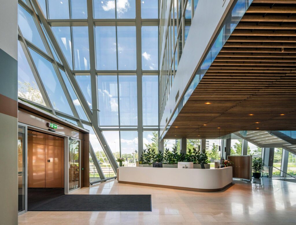 Moderne ontvangsthal met glazen gevel, houten plafond en een receptiebalie aan de David Ricardostraat.